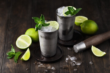 Mojito cocktail with lime, mint and crushed ice on dark wooden background. Side view