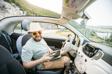 Hipster man looking on location navigation map in car, tourist traveler driving and hold in male...