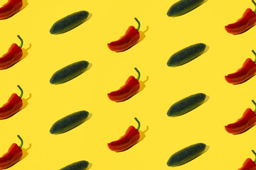 Red pepper and cucumber arranged on a yellow pastel background.
