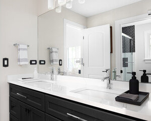 A bathroom with a black cabinet, white marble countertop with two sinks, and a view of the shower in the reflection.