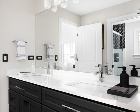 A bathroom with a black cabinet, white marble countertop with two sinks, and a view of the shower in the reflection.
