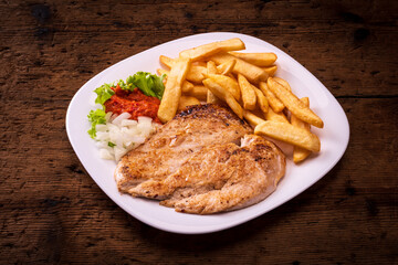 plate with chicken breast and french fries on wooden table