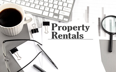 PROPERTY RENTALS text on a paper with magnifier, coffee and keyboard on grey background