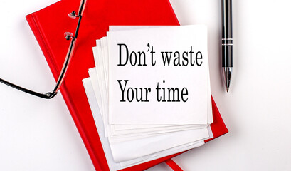 DON'T WASTE YOUR TIME text on sticker on red notebook with pen and glasses
