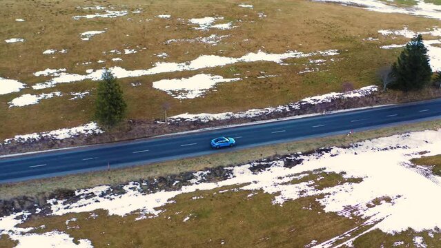 A blue Audi S3 driving along a mountain straight road in winter, cinematic shot from a drone in the Polish Tatra Mountains.