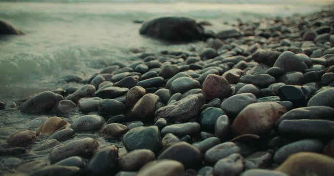 Clear Waves Splashing Against Stony Beach Shore with Colorful Rocks. Coastal Rising Tide Rocky Erosion Closeup in Slow Motion. Cinematic Ocean Lake 4k
