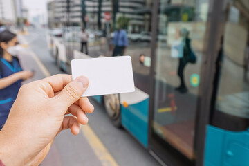 Credit or prepaid transport card in the passenger's hand against the background of a modern city bus at city street