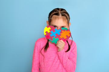 A shy child with autism syndrome hides behind a heart-shaped card with colorful puzzles inside.