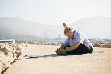 Fototapeta na wymiar Mature woman with dreadlocks working out doing yoga exercises on sea beach copy space - wellness well-being and active elderly age concept
