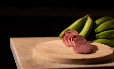 salami slices on a cutting board, with green bananas in the background country style
