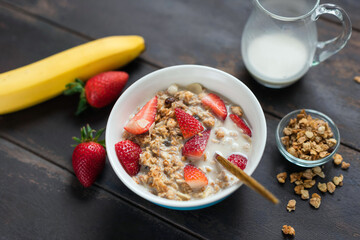 Granola bowl with strawberries and alternative oat milk on a wooden table background