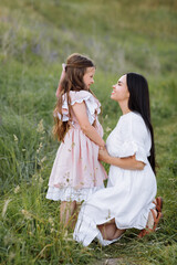 Fototapeta premium Mothers Day, Women's day. Happy young beautiful mother is hugging her little daughter in the green meadow on summer day. Mom with child are spending time together on nature. World Children day.