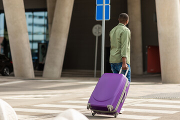 Fototapeta na wymiar Black Guy Walking With Travel Suitcase At Airport, Back View