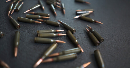 Scattered on a dark surface are bullets, cartridges for a kalashnikov assault rifle. - obrazy, fototapety, plakaty
