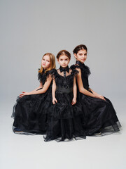 three cute girls in a black long curvy dress on a gray background. 