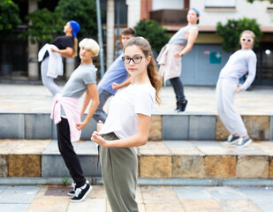 Obraz premium Confident teen girl street dancer posing during performance with group in summer city .