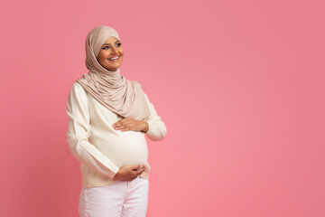 Pregnant muslim woman in hijab embracing her belly and looking away