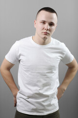 Studio portrait of handsome confident young man in casual white t shirts with mock up crossed his hands and looking at camera isolated on grey background.