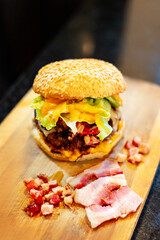 meat burger, with cheddar cheese and bacon on wooden board with black background.