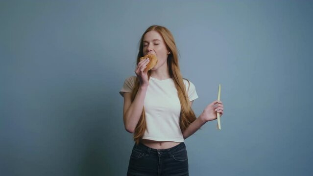 Woman enjoying delicious burger closing eyes from pleasure, having good appetite isolated over gary background. Hungry woman indoor