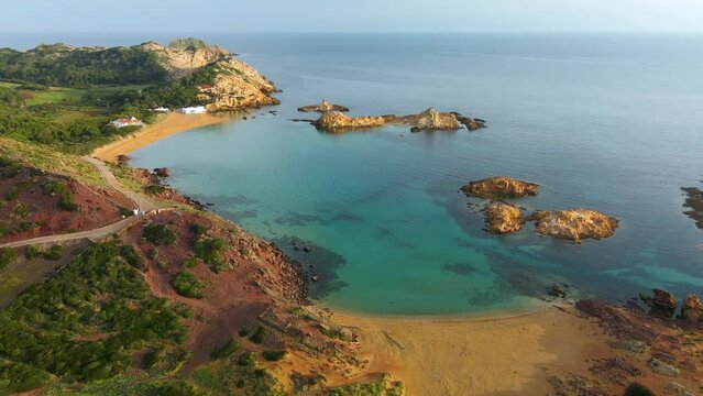 Cala Pregonda virgin beach in Menorca with golden glow of sunset lighting up the cliff edge.