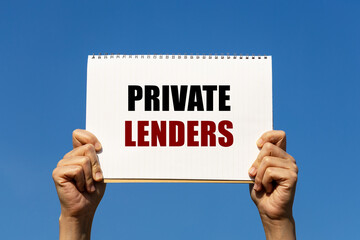 Private lenders text on notebook paper held by 2 hands with isolated blue sky background. This message can be used as business concept about private lenders.