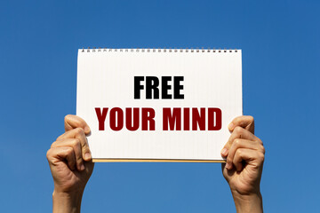 Free your mind text on notebook paper held by 2 hands with isolated blue sky background. This message can be used as business concept about meditation.