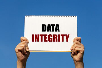 Data integrity text on notebook paper held by 2 hands with isolated blue sky background. This message can be used as business concept about data security.