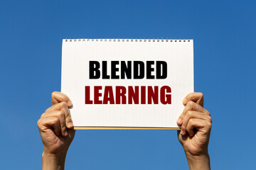 Blended learning text on notebook paper held by 2 hands with isolated blue sky background. This message can be used as business concept about blended learning.