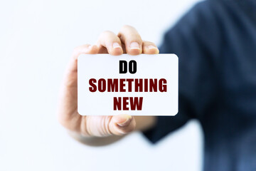 Do something new on blank business card being held by a woman's hand with blurred background. Business concept about doing new thing.