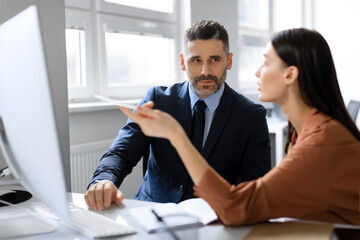 Middle aged businessman and his female colleague working together, using computer in office, preparing business project