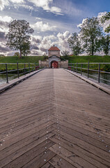 Copenhagen, Denmark - September 13, 2010: North entrance  of Kastellet citadel over wooden bridge spanning moat leading to green ramparts and gate tower under blue cloudscape