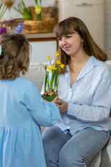 Fototapeta na wymiar Cute little girl, baby daughter giving pink tulip flowers to her happy young beautiful mom. Celebration of Mother's or Women's day, birthday or anniversary. Cozy home atmopshere, kitchen. Springtime