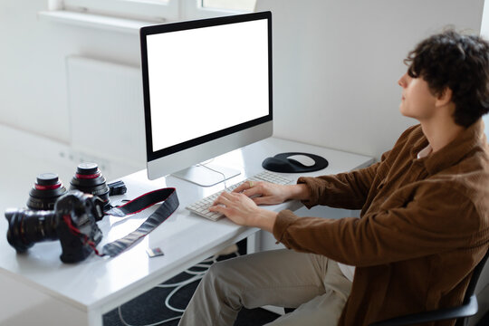 Male graphic designer or photographer working with empty screen computer at workspace, sitting at desk with equipment