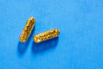 Two pills filled with gold glitter on blue background. C