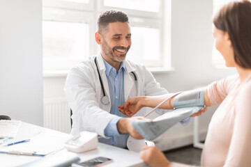 Gestational hypertension. Male doctor measuring arterial blood pressure of young pregnant lady...