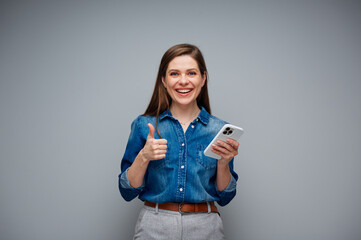 Woman using smartphone and showing thumb up. Portrait of smiling girl on gray back.