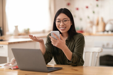 Impressed asian woman looking at smartphone screen at home