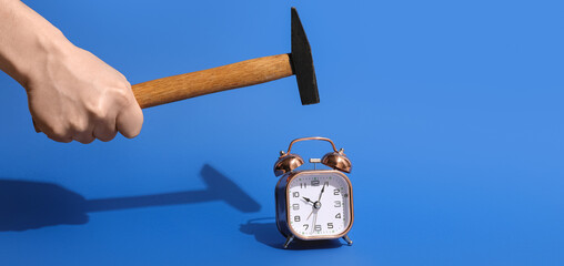 Human hand with hammer and alarm clock on blue background © Pixel-Shot