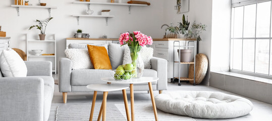 Basket with fresh apples and vase with tulips on table in light room