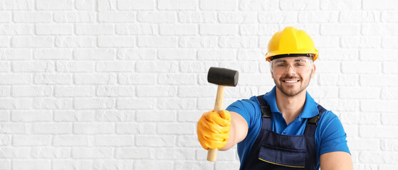 Male worker with rubber hammer on white brick background with space for text