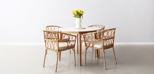 Vase with yellow tulips on dining table and wicker chairs in light room