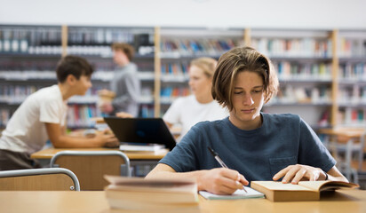 Portrait of teenager reading books and writing in notebooks in the library