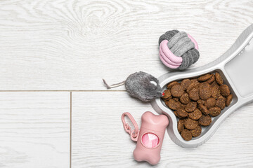 Fototapeta na wymiar Bowl of dry pet food, waste bags and toys on light wooden background