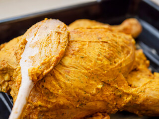 Raw uncooked full chicken on a metal cooking tray in yellow lemon and mustard marinade ready to be cooked in an oven. Fresh poultry product.