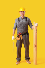 Mature carpenter with hacksaw and wooden plank on yellow background