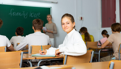 Obraz premium Teenage girl turned around and looking at camera during lesson in classroom.