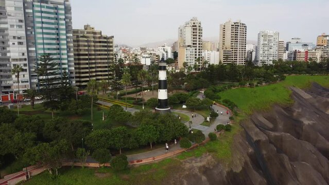 Black and white colored lighthouse in public park near coastal cliff's edge. Many trees and green grass surround the lighthouse called "Faro de la Marina" Located in Miraflores district of Lima, Peru.