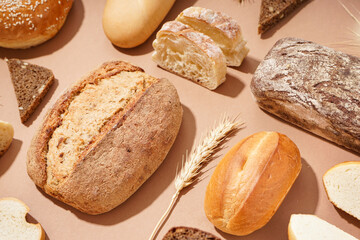 Fresh loaves of different bread and wheat ears on brown background