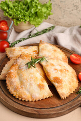 Wooden board with baked meat empanadas on table, closeup